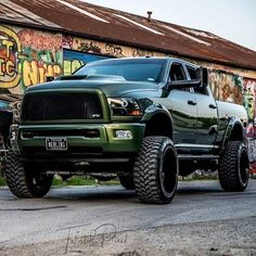 a green ram truck parked in front of a building with graffiti on the wall behind it