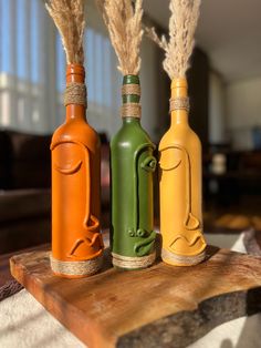 three different colored bottles sitting on top of a wooden table next to some dry grass