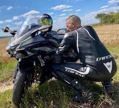 a man sitting on the ground next to a motorcycle in front of a wheat field