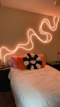 a bed with white sheets and pillows in front of a wall that has neon lights on it