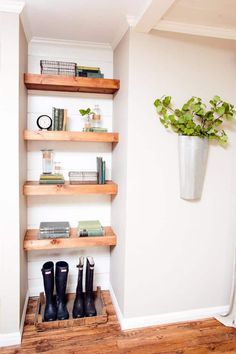 a pair of black rain boots sitting on top of a wooden shelf next to a potted plant