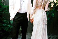 a bride and groom hold hands as they stand in front of a wooden wall with greenery