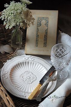 a table setting with flowers in a vase and an empty book on the table next to it