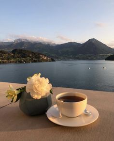 a cup of coffee sitting on top of a table next to a vase filled with flowers