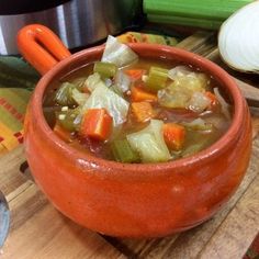 a bowl of soup with carrots, celery and onions on a cutting board