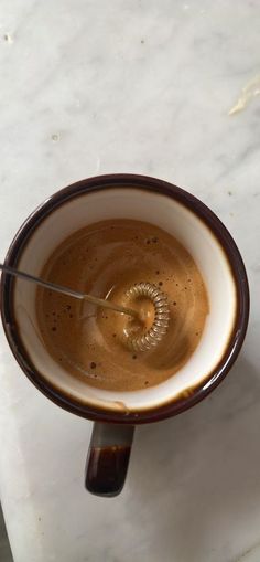 a brown and white coffee cup sitting on top of a marble counter next to a spoon