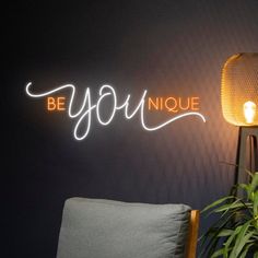 a neon sign that says be you on the wall next to a chair and lamp