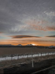 the sun is setting over an open field with mountains in the distance and snow on the ground