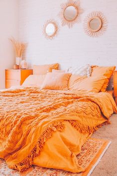 a bed with orange sheets and pillows in a bedroom next to two round mirrors on the wall