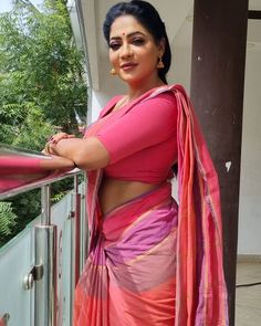 a woman in a pink and orange sari standing on a balcony with her arms crossed