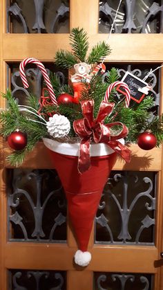 a red vase filled with candy canes and greenery on top of a wooden door