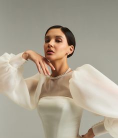 a woman in a white dress posing with her hands on her hips and arms behind her head