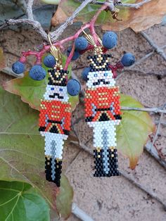 two beaded nutcrackers hanging from a tree branch with berries on it