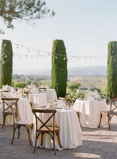 an outdoor dining area with tables and chairs covered in white tablecloths, surrounded by greenery