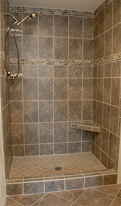 a walk in shower sitting next to a tiled wall and floor covered in brown tile