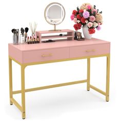 a pink desk with flowers and makeup on it, next to a mirror that has a gold frame