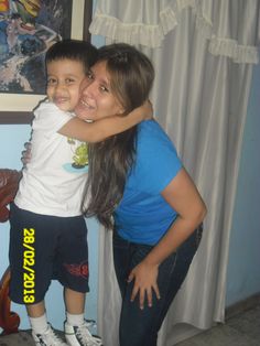 a woman hugging a young boy in front of a window with curtains behind him and a painting on the wall