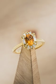 an orange and white diamond ring sitting on top of a wooden stand in front of a beige background