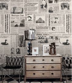 an old dresser is in front of a wall with newspapers on it and a lamp next to it