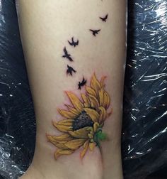 a sunflower with birds flying around it on the side of a woman's leg