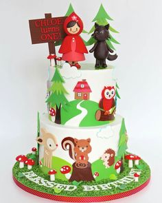 a three tiered cake with animals and trees on it's sides, topped with a sign that says gloof tups one