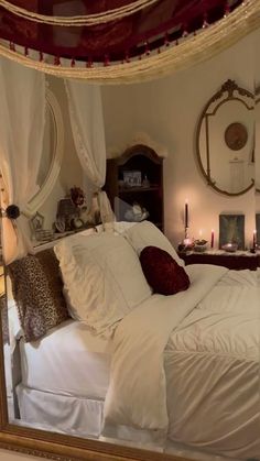 a bed with white sheets and pillows in front of a mirror that has candles on it