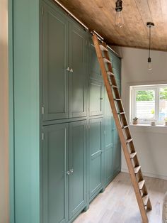 a ladder is hanging from the ceiling in a room with green cabinets and wood floors