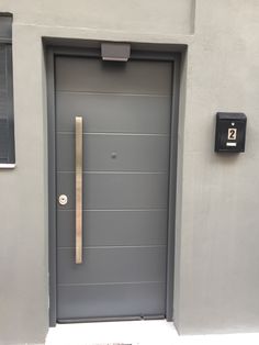 a grey door with a metal handle on the side of a gray building in front of a black mailbox