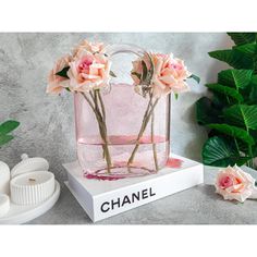 two pink flowers in a clear bag with the word chanel on it next to some plants