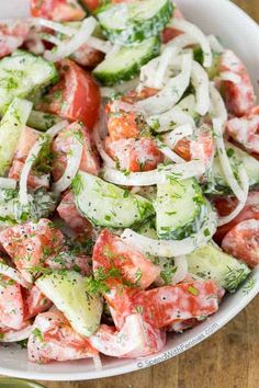 a salad with cucumbers, tomatoes and onions in a white bowl on a wooden table