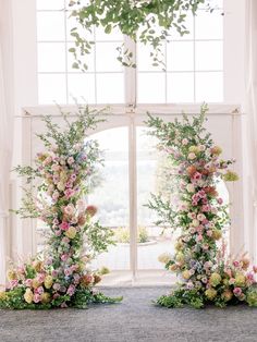 an arch with flowers and greenery in front of a window