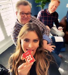 a woman holding up a piece of cake to her face while two men look on