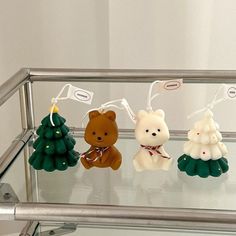 three small teddy bears sitting on top of a glass shelf next to christmas tree ornaments