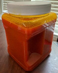 a plastic container filled with liquid sitting on top of a wooden table next to a window