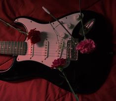 an electric guitar with flowers on it laying on a red sheet in the middle of a bed