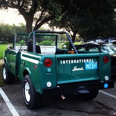 a green pick up truck parked in a parking lot next to other cars and trees