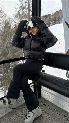 a woman sitting on top of a metal rail in front of a window next to snow covered ground