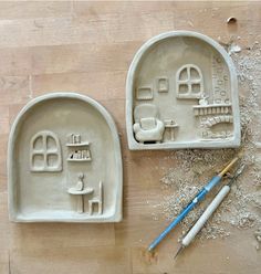 two clay molds sitting on top of a wooden table next to paintbrushes