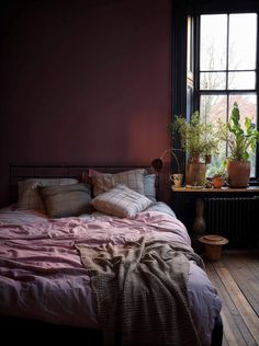 a bed sitting in front of a window next to a table with potted plants