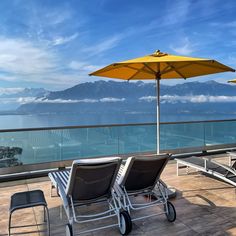 two lounge chairs and an umbrella on a balcony overlooking the ocean with mountains in the background