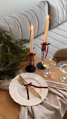 a table set for christmas with candles and wine glasses on it, next to a couch