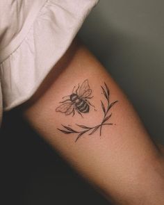 a woman's arm with a small tattoo of a bee and flowers on it