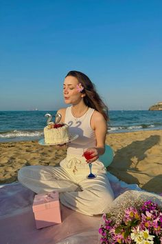 a woman sitting on the beach with a cake and wine glass in front of her