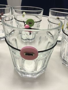 several glass cups on a table with little figurines in the middle one has a pink button