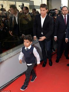 a young boy in a suit and tie walking down a red carpeted area with photographers behind him