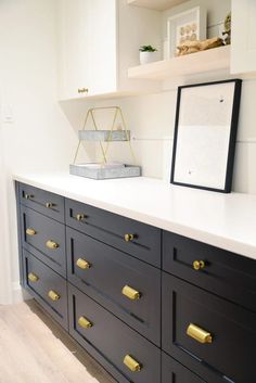 a black and white dresser with gold handles in a room that has shelving on the wall