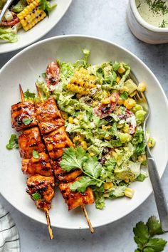 two plates with chicken, lettuce and corn on skewered skewers