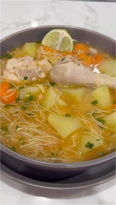 a bowl of chicken noodle soup with carrots, celery and lemon