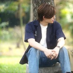 a young man sitting on top of a stone bench next to a tree in a park