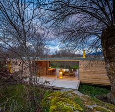 an outdoor deck with table and chairs next to trees in the woods at night time